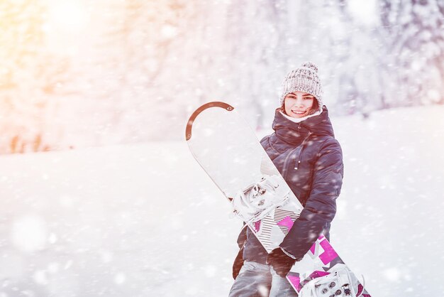 Snowboarding on a winter day A young woman with her snowboard on a white slope She is having fun and feeling the adrenaline Stunning background view of the snowcovered pines Girl in winter