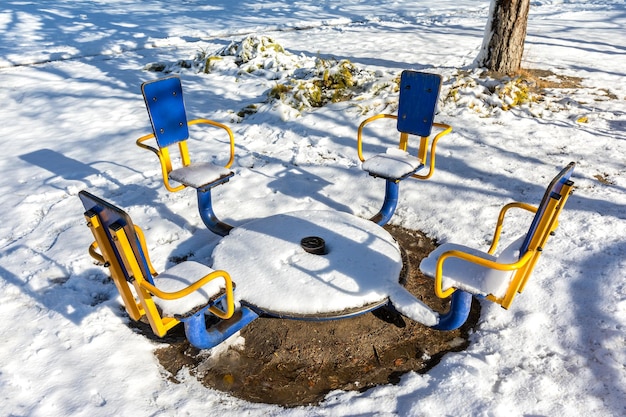 雪に覆われた子供用カルーセルが明るい太陽の下で溶ける冬の公園の都会の風景