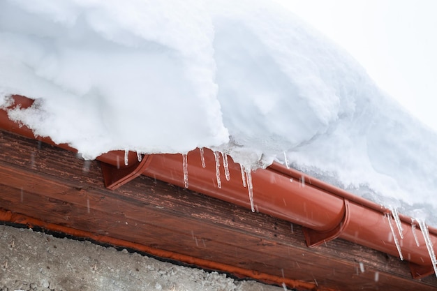 A snowdrift on the roof of a house from which icicles hang Cleaning roofs from accumulated snow