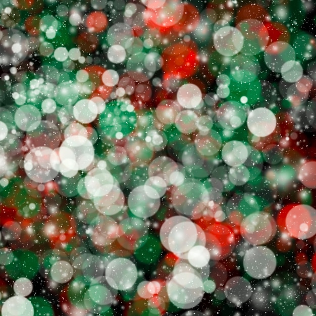 緑の赤いボケ味の背景に降雪。クリスマスの背景。