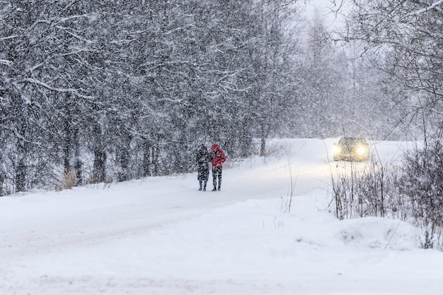 Snowfall in winter a winter day people are walking on the road m passing car Falling snow on a blurry nature background