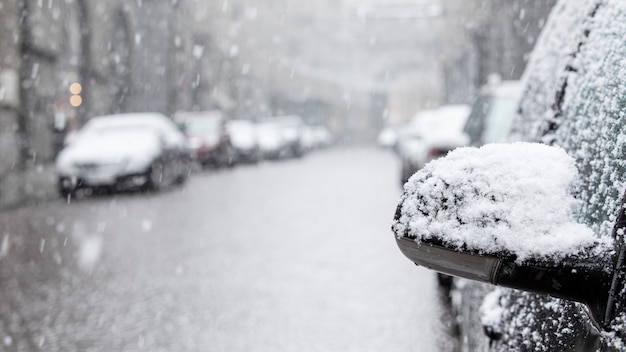 Snowflakes fall on a car mirror on a winter city street. Snowfall or blizzard.