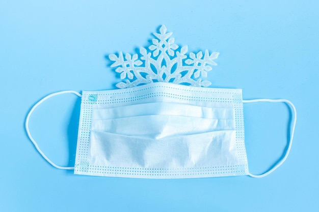 Snowflakes and medical protective mask with golden ribbon isolated on blue background. A gift for Christmas and New Year 2021. Coronavirus pandemic concept.