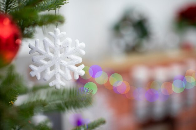 На ветке рождественской елки висит украшение в форме снежинки