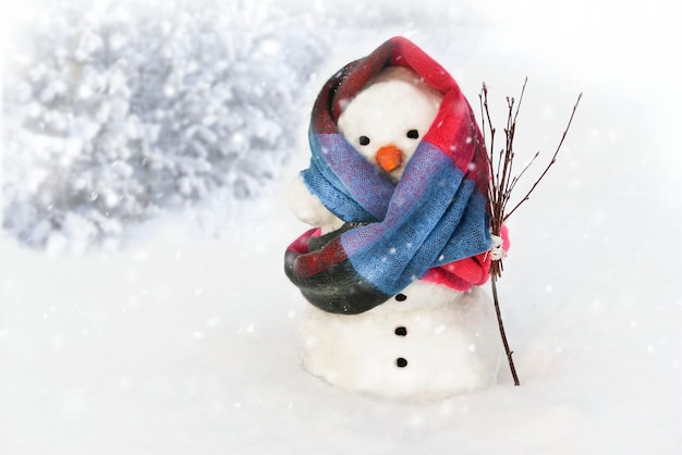 A snowman in a beautiful scarf stands in the forest with a broom and snow elements