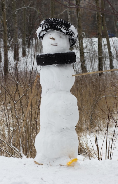 Фото Снеговик, украшенный автомобильными шинами вместо шапки и шарфа в зимнем парке
