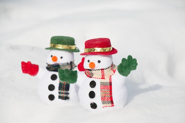 Снеговик и друг стоят среди кучи снега в парке. Утреннее солнышко зимой согревает. Добро пожаловать в рождественский сезон.