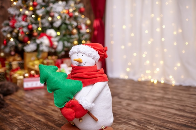 A snowman holds a Christmas tree