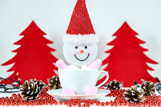 Snowman and marshmallows in cup red felt christmas tree on white background