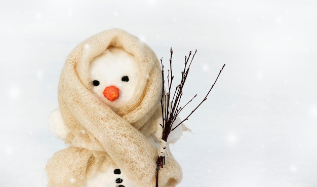 Photo a snowman in a white scarf on a light background holds a broom