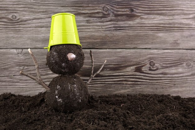 Snowman with a green pot made from soil without snow.