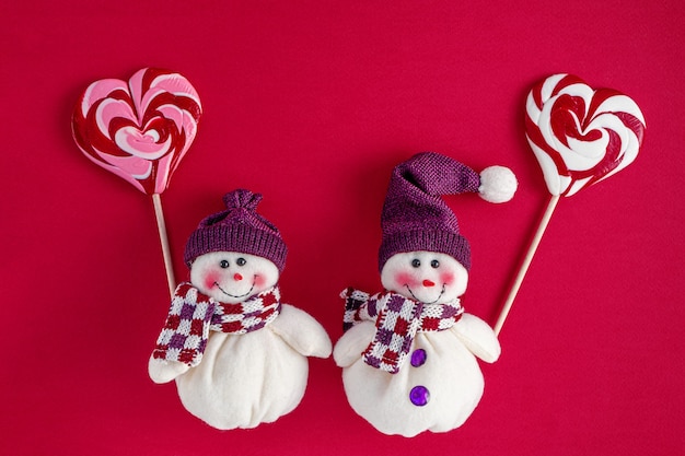 Снеговики держат традиционные рождественские конфеты в форме сердца
