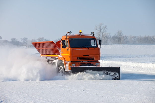 Snowplow is cleaning a road and snow flying around it