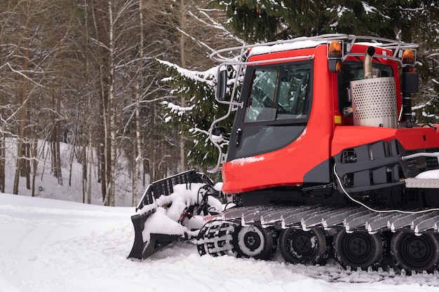 納屋の近くの森で冬に立っている赤いトラックの除雪車