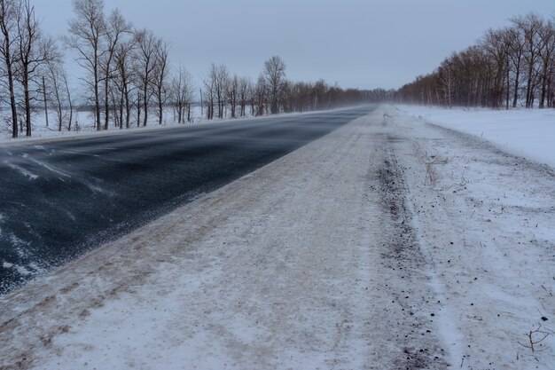 Photo snowstorm on the highway. patterns on the winter highway in the form of four straight lines. snowy road on the background of snow-covered forest.