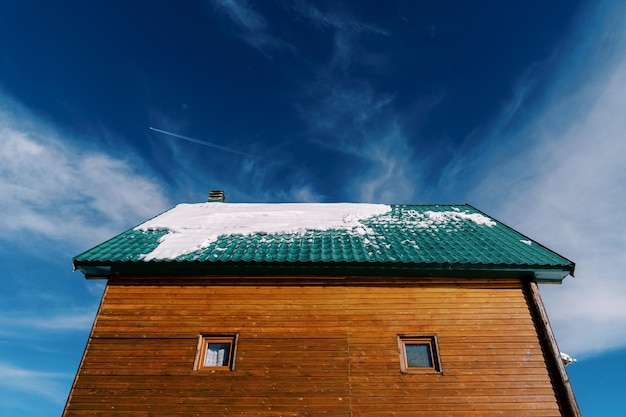 Snowy green tiled roof of a wooden cottage against a blue sky