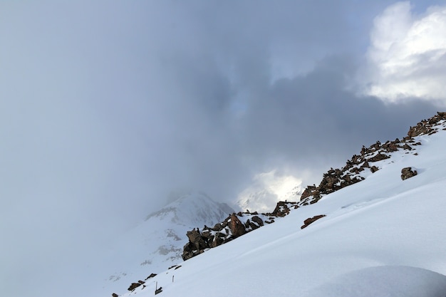 Snowy mountain side with big stones and birds in the clouds