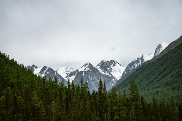 Snowy mountain top between big mountains under overcast sky. 