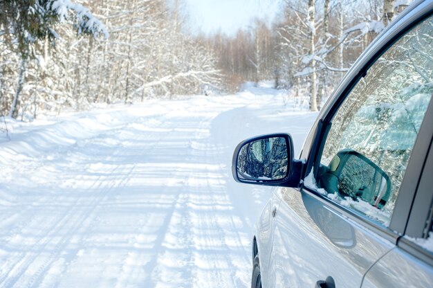 Strada innevata. lato di una macchina con uno specchio. bosco innevato nel pomeriggio