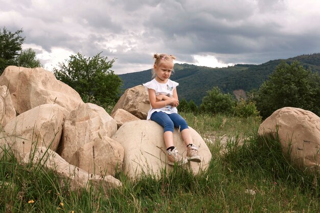 Snurkend meisje zittend op een grote steen op een achtergrond van bergen