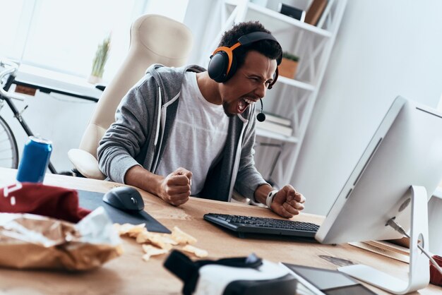 So angry! Furious young man in casual clothing using computer and shouting while spending time at home