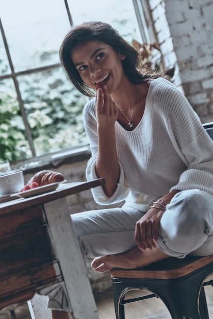 Photo so delicious! attractive young woman looking away and eating strawberry