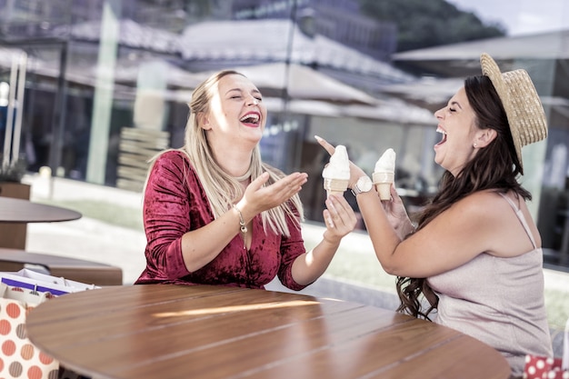 So funny. Joyful happy woman pointing at her friend while eating ice cream