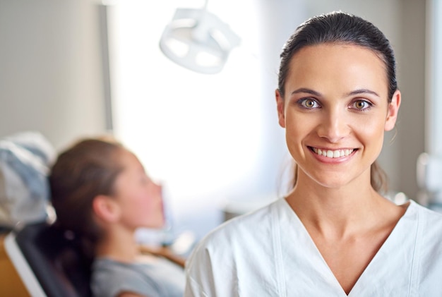 Foto sono così felice di aver deciso di specializzarmi in odontoiatria una dentista donna in piedi nel suo studio con il suo bambino paziente sullo sfondo