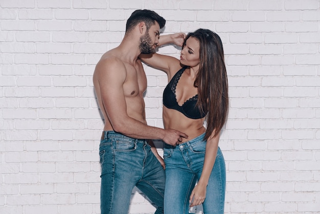 So good to be in love! Beautiful young couple looking at each other while standing against brick wall