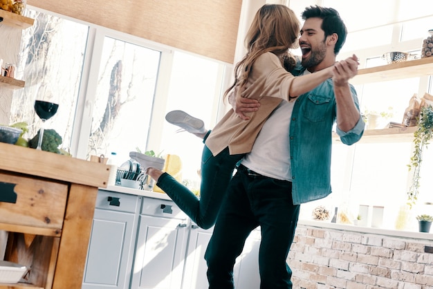 So great to be together! Full length of beautiful young couple in casual clothing dancing and smiling while standing in the kitchen at home