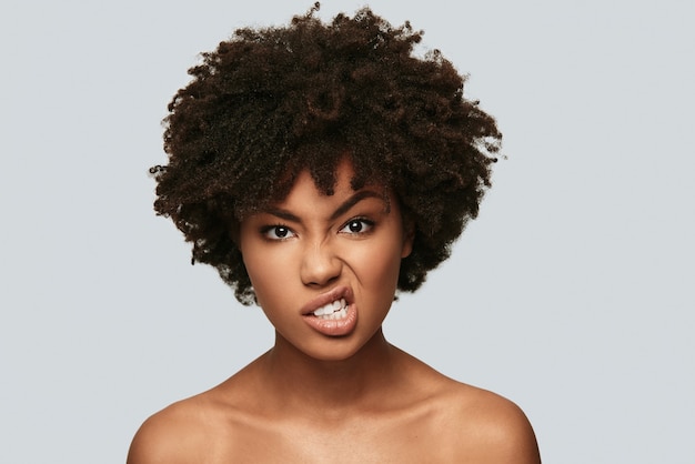 So mad! Displeased young African woman looking at camera and making a face while standing against grey background