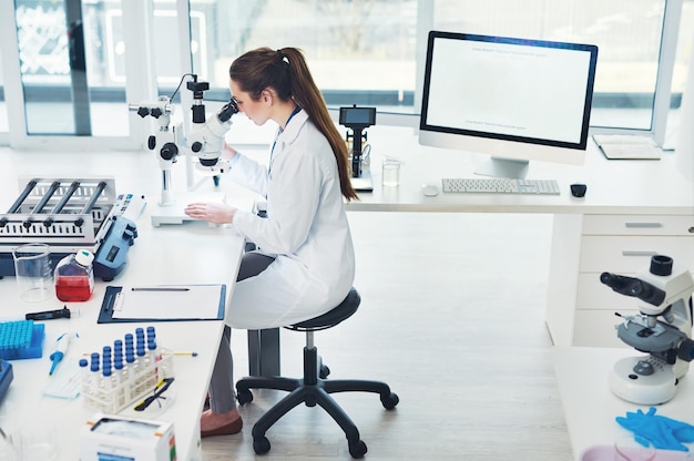 研究室の中でテストをしている間、顕微鏡を通して見ている焦点を合わせた若い女性科学者のトリミングされたショットをするためにまだ多くの仕事があります