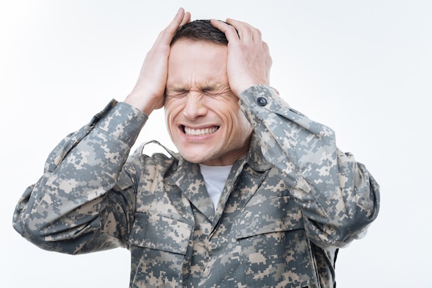 So stressed out. Unhappy cheerless military man closing his eyes and holding his head while being stressed out