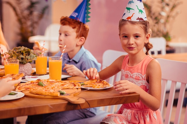 Così dolce. piccola femmina allegra mantenendo il sorriso sul viso mentre si mangia la pizza