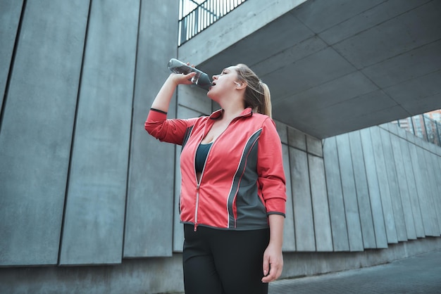 だから、運動をしながら水を飲むスポーツ服の喉が渇いた若い魅力的なプラスサイズの女性