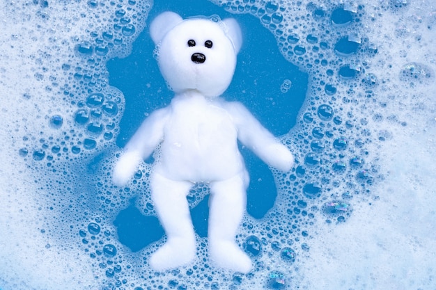 Soaking bear toy in laundry detergent water dissolution before washing. Laundry concept.