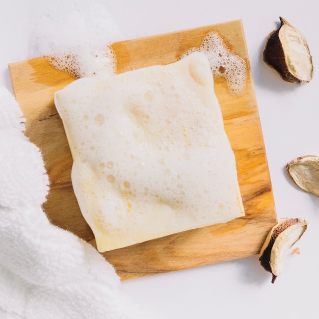 Photo soap bar with foam on wooden board near towel and cotton pods