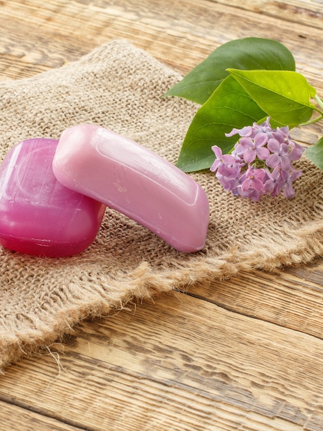 Soap for bathroom procedures and lilac flowers on sackcloth and old wooden boards. Spa products and accessories.