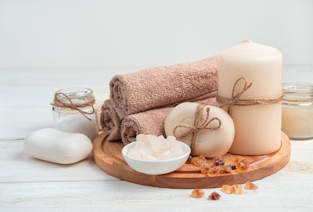 Soap, candles, towel and salt on a board on a white wooden background. The side view is horizontal. The concept of spa treatments.