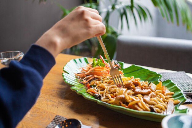 Soba udon Aziatische tarwenoedels met kip en groenten in groene plaat Vrouw eet met vork