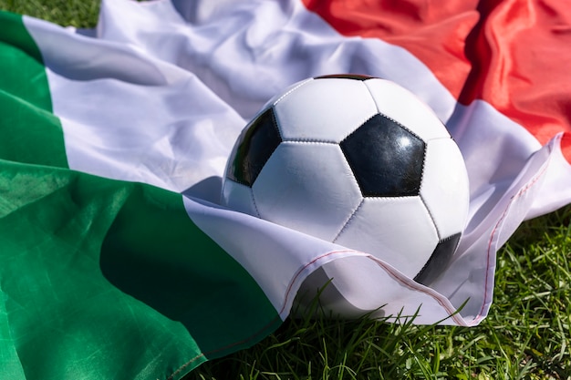 Foto pallone da calcio sullo sfondo della bandiera italiana che fluttua nel vento sull'erba verde campioni europei green