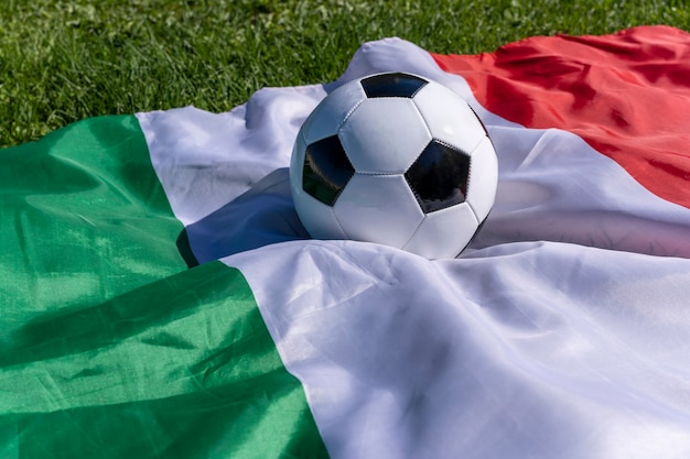 Футбольный мяч на фоне итальянского флага, развевающегося на ветру на зеленой траве европейских чемпионов