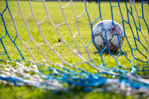 Soccer ball on field background Behind view of net and football leather ball on green grass