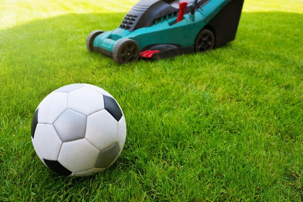 Soccer ball and lawn mower on a field in the grass close-up grass care