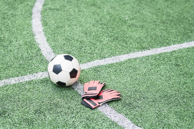 Soccer ball and leather gloves of football player on crossed white lines of green empty field for trainings and matches