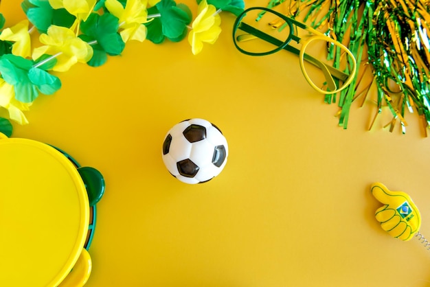 Soccer ball and some brazilian fan items on yellow background