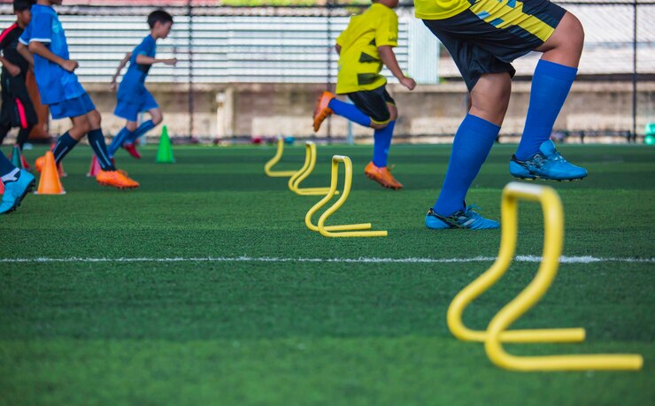 サッカーアカデミーで子供たちのジャンプスキルを訓練するためのバリアコーンを備えた芝生のフィールドでのサッカーボールの戦術
