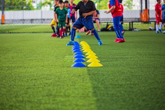 Tattiche di pallone da calcio sul campo in erba con cono di barriera per addestrare i bambini a saltare l'abilità nell'accademia di calcio