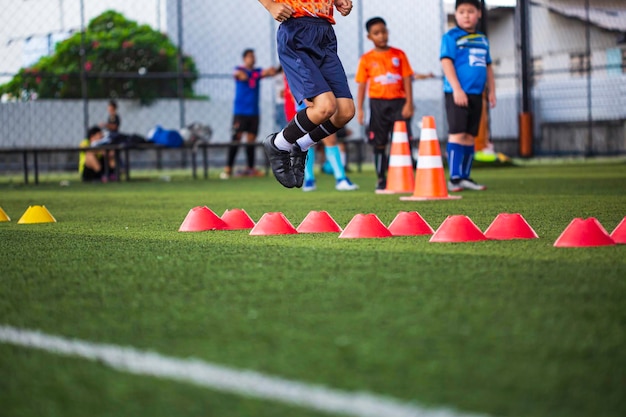 子供たちのジャンプスキルを訓練するための障壁を持つ芝生のフィールドでのサッカーボールの戦術