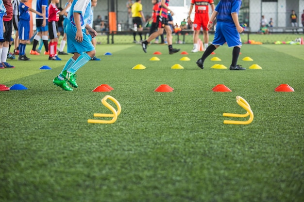 サッカーアカデミーで子供たちのジャンプスキルを訓練するためのコーンを備えた芝生のフィールドでのサッカーボールの戦術